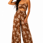 A woman modeling a brown two-piece set featuring a strapless bandeau top with a twisted front and matching wide-leg pants, both in a brown and beige floral print, against a plain white background.