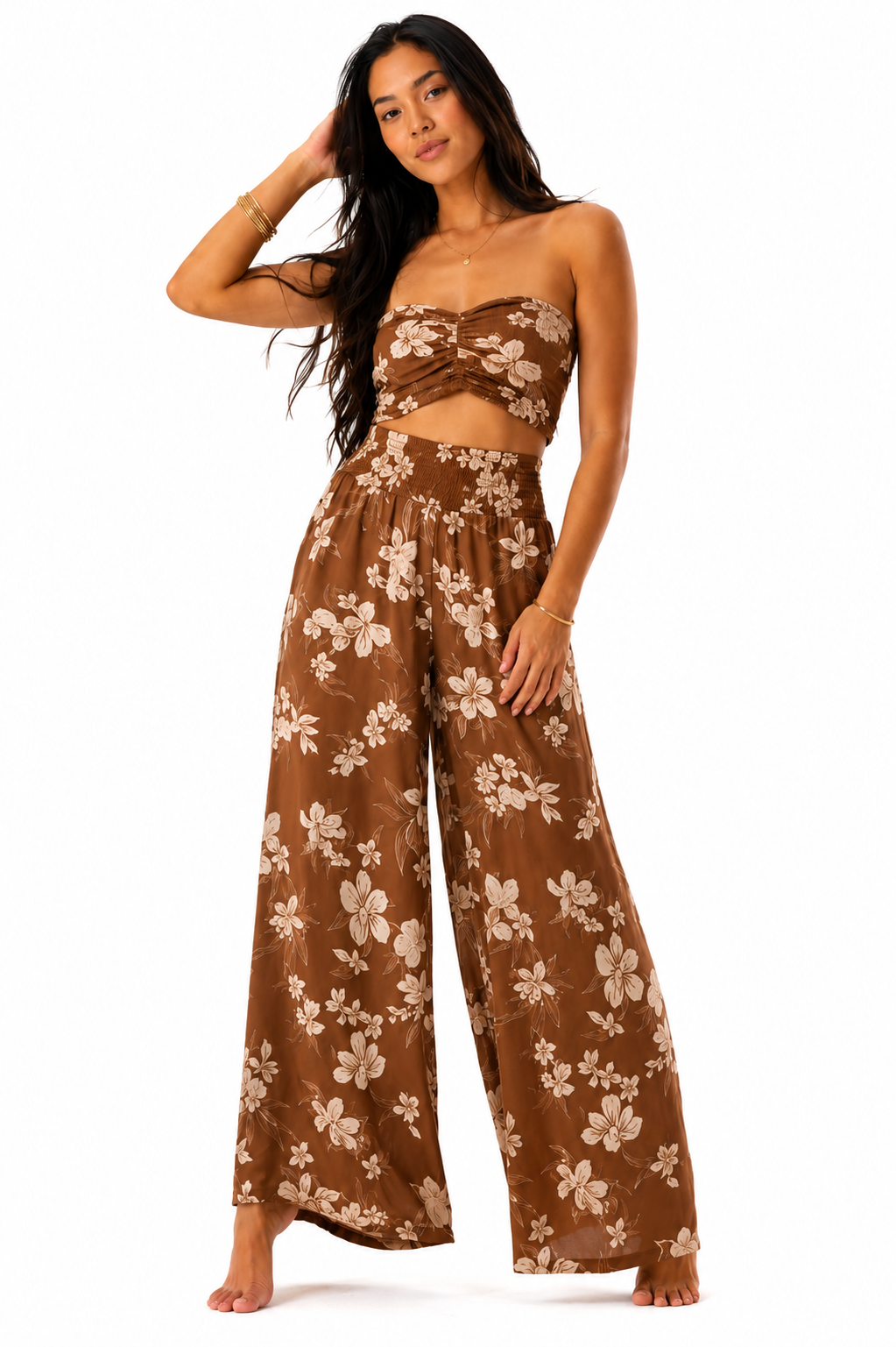 A woman modeling a brown two-piece set featuring a strapless bandeau top with a twisted front and matching wide-leg pants, both in a brown and beige floral print, against a plain white background.