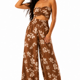 A woman modeling a brown two-piece set featuring a strapless bandeau top with a twisted front and matching wide-leg pants, both in a brown and beige floral print, against a plain white background.