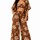A woman modeling a matching brown floral lounge set consisting of a bandeau crop top, wide-leg pants, and a short-sleeve open-front cover-up, set against a plain white background.