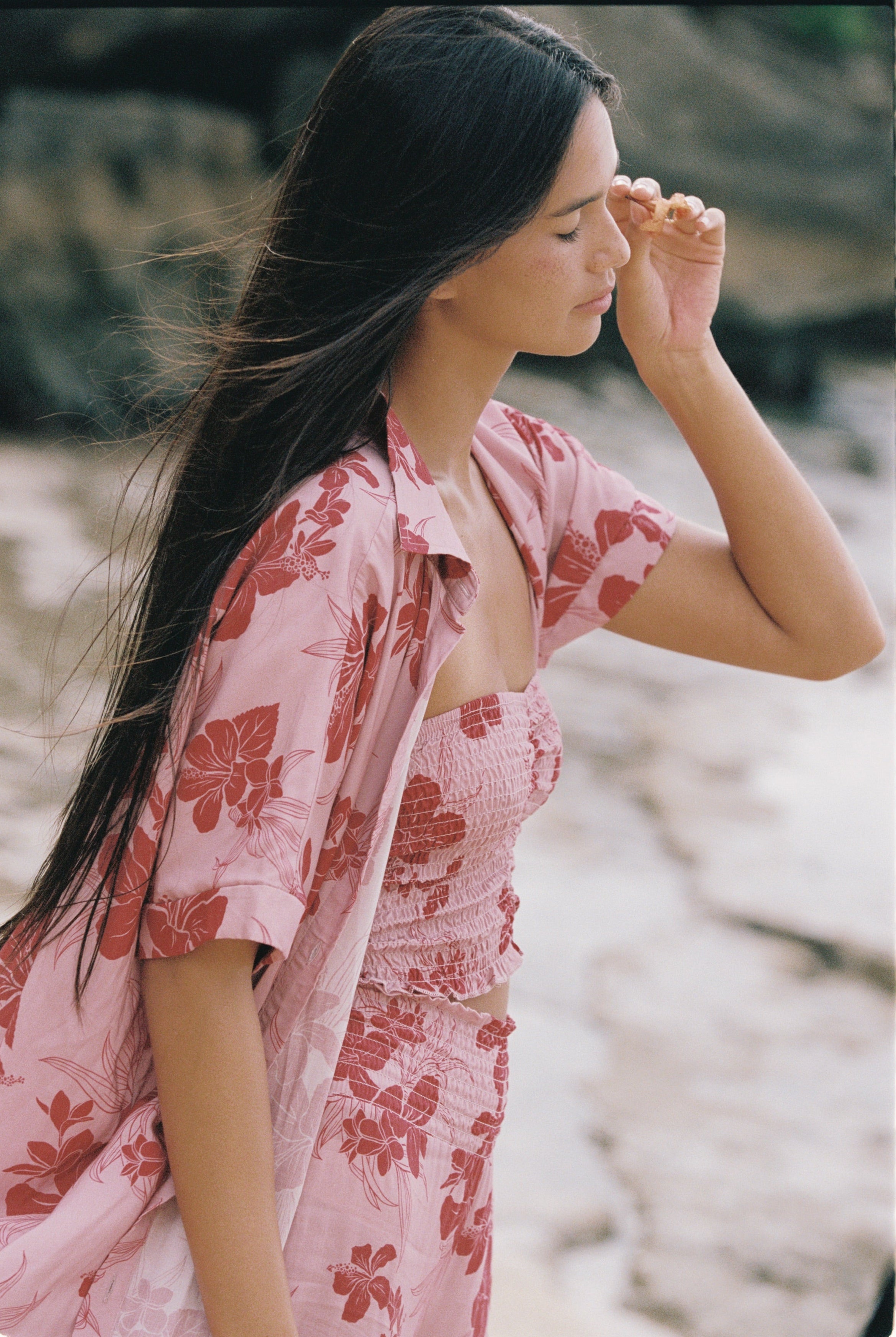 A woman wearing the solstice shirt by Guava & Co, a pink floral two-piece set with a matching open shirt, standing outdoors.