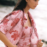 A woman wearing a pink floral two-piece set with a matching open-front robe, posed outdoors against a soft-focus natural background.